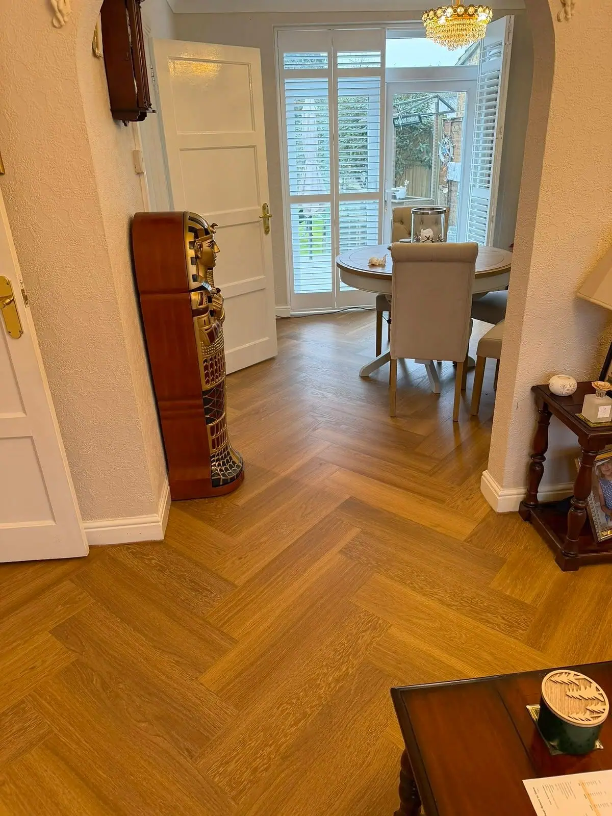Honey-toned herringbone floor running from a hallway into a dining room