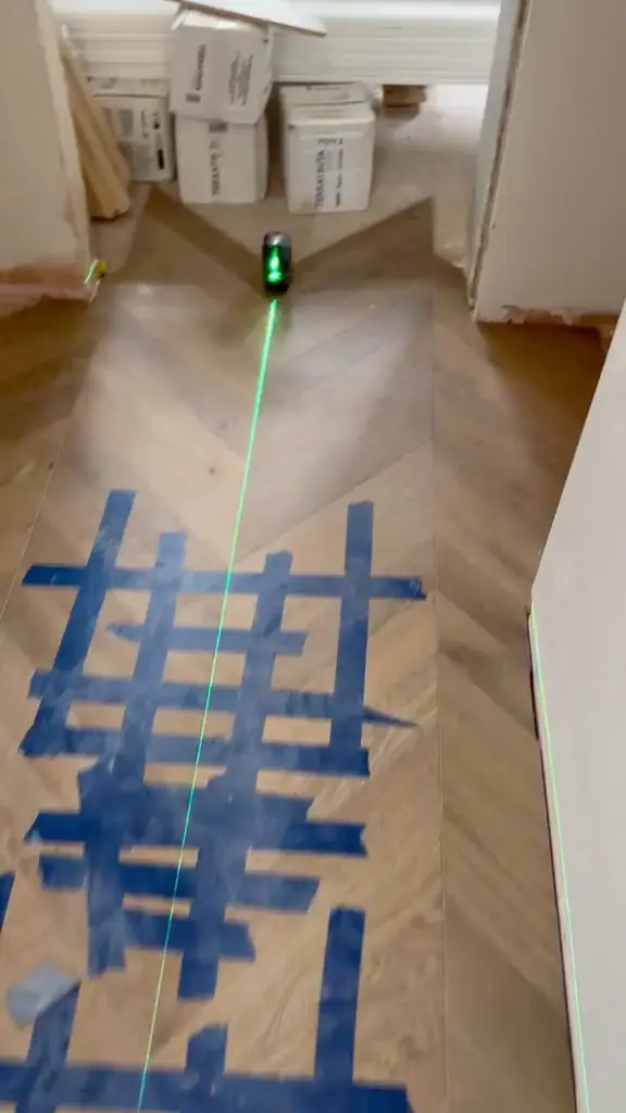 A laser line running down the centre of a chevron floor part-way through fitting