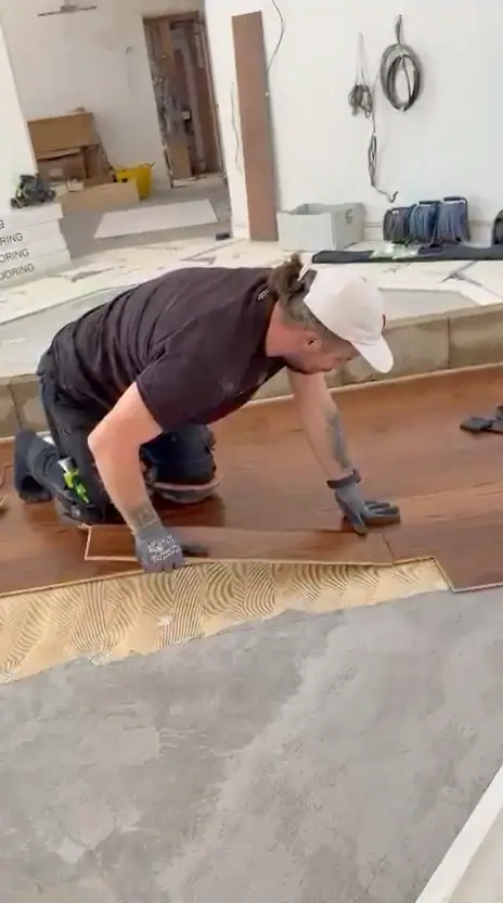 Alex, in a white cap, fitting a board into place on a part-laid floor