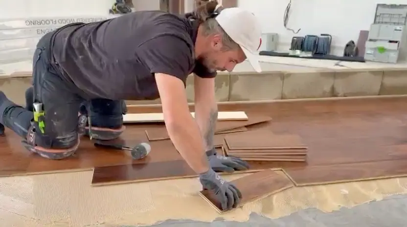 Alex pressing a board down into fresh adhesive on a part-laid floor