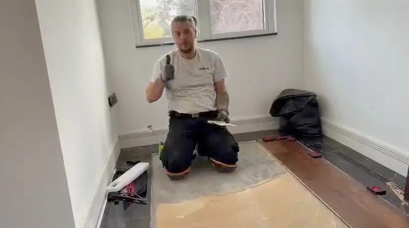 Alex kneeling beside a freshly spread bed of adhesive, giving a thumbs up