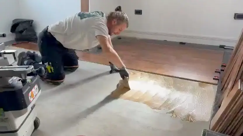 Alex spreading flooring adhesive with a trowel beside the boards already laid